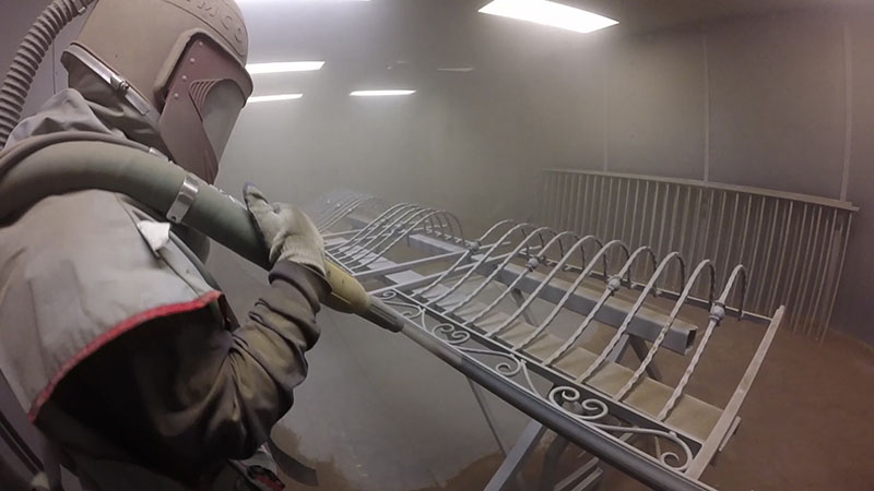 man in full gear, sand blasting a rail.